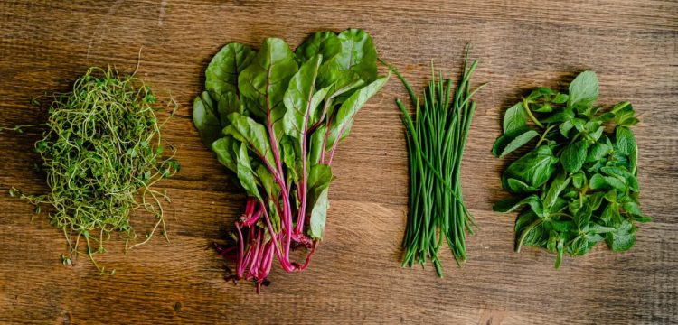 A vibrant selection of fresh herbs and greens neatly arranged on a wooden tabletop.