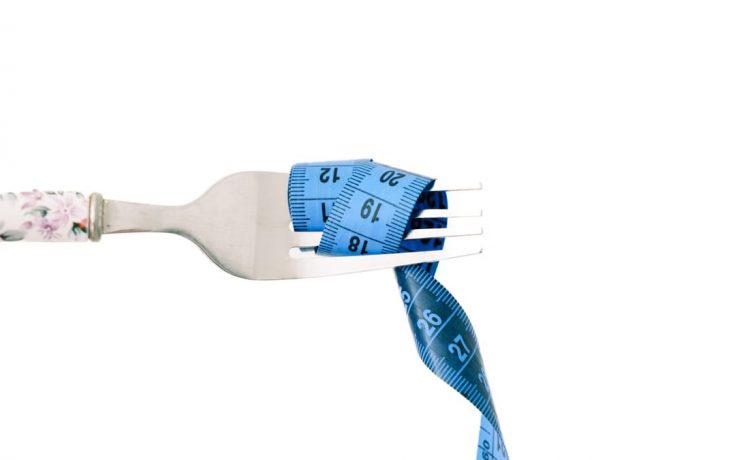 A close-up of a fork wrapped in blue measuring tape, symbolizing diet and weight management.